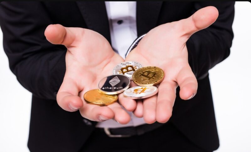 Muškarac u crnom odelu drži na otvorenim dlanovima nekoliko fizičkih kovanica sa simbolima Bitcoina i Ethereuma